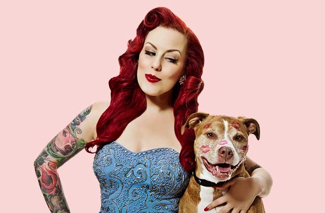 Dog's best friend - Red haired woman with tattooed arm holding dog with lipstick kisses on face